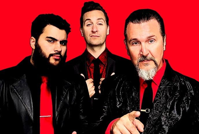 The 3 band members of Big Sugar posing for the camera, wearing black and red attire in front of a red background.