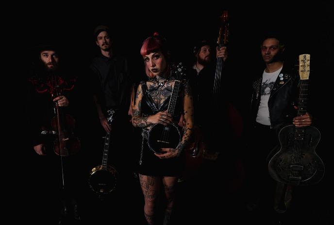 The Bridge City Sinners pose with a violin, banjo, upright bass, and guitar against a dark background.