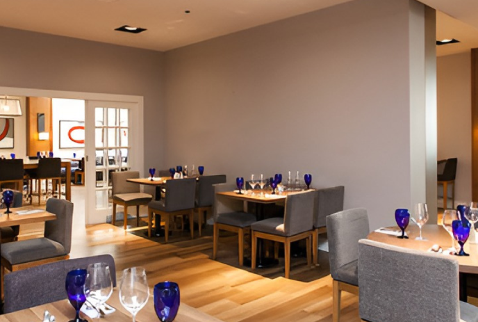Modern dining room with wooden tables, gray chairs, and neatly set glasses in a bright open space.