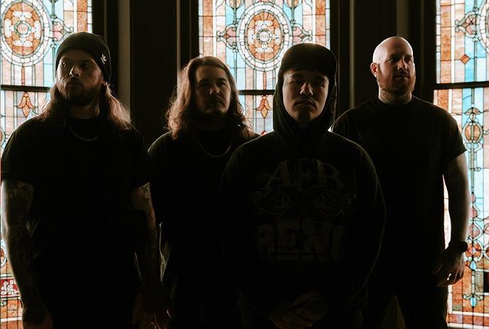 The band Bodysnatcher stands in front of a colorful stained glass window, dressed in dark clothing.