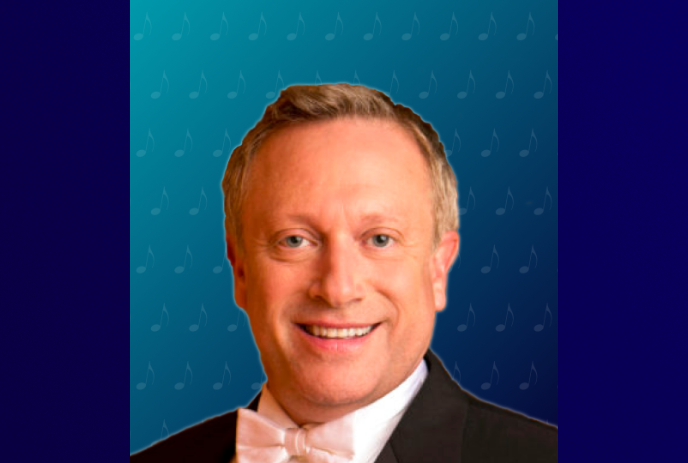 A smiling artist in a tuxedo stands before a blue backdrop decorated with musical notes.