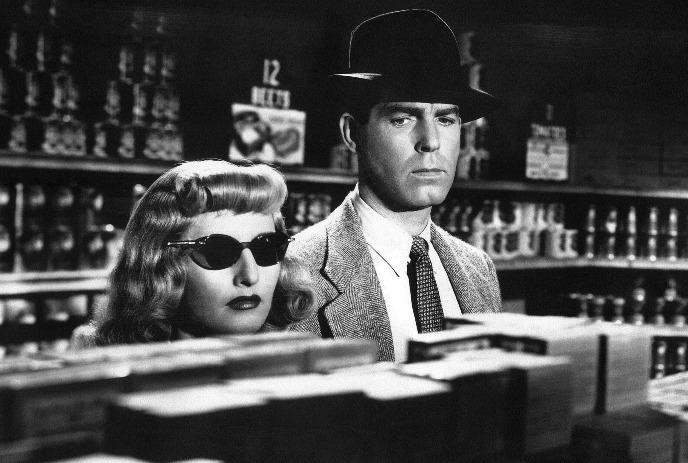 Black and white image of a man and a woman standing at a counter looking devious.