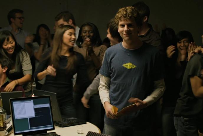 Group of young people standing together around a computer.