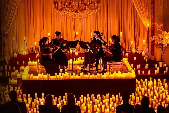 Four people sit onstage with their instruments while surrounded by candlelight giving off an orange glow.