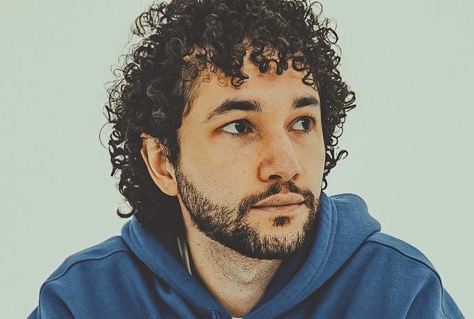 CapoChino with curly hair and beard in a white and red shirt dances joyfully while mixing music on a console.