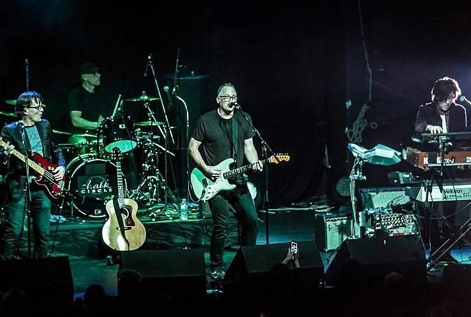 Chalk Circle performing live on stage with guitar bass drums and keyboards under dim green blue concert lighting.