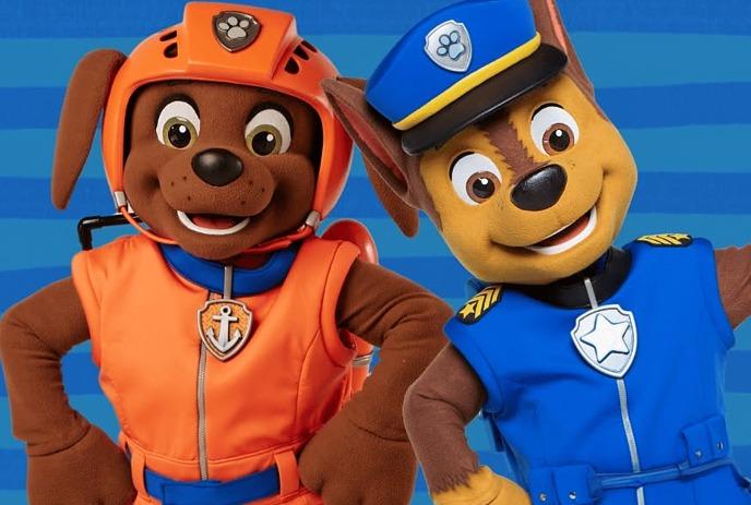 Two costumed PAW Patrol characters, Zuma in orange and Chase in blue, stand smiling under blue background.