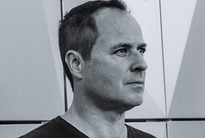 A black-and-white portrait of Christian Smith looking forward against a structured, dark slatted wall.