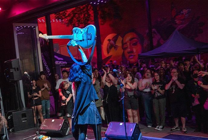 People gather under colorful lights and a mural, enjoying an outdoor urban event with lively ambiance.