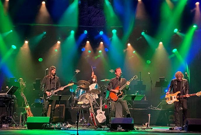 Classic Albums Live band performs on stage with colorful lighting, featuring musicians playing instruments.