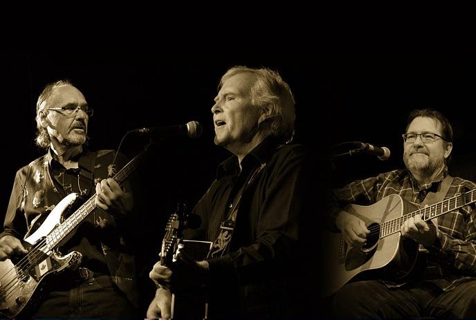 A black and white photo of Gordon Lightfoot playing a guitar on stage with his eyes closed.