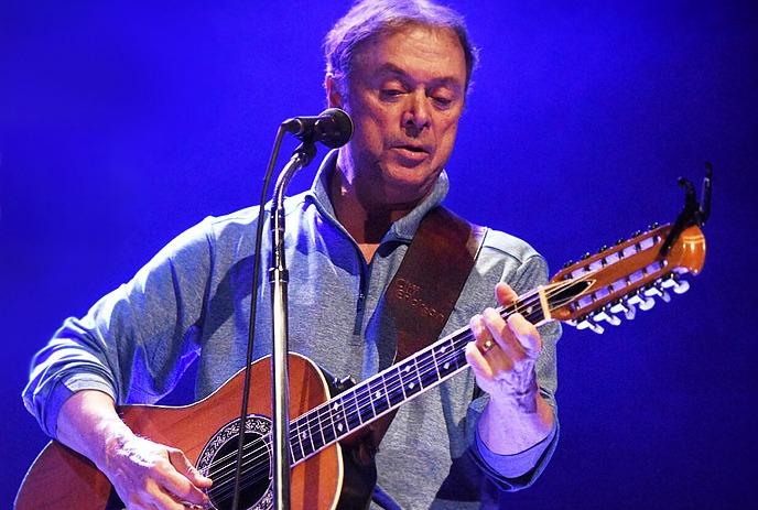 Cliff Erickson performing on stage with a guitar in front of a blue background.