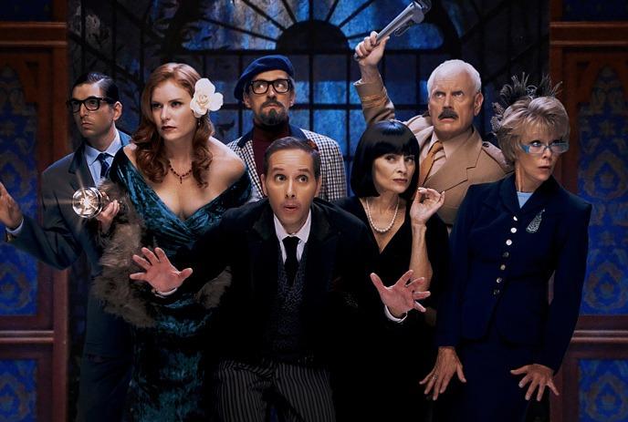 A lively group of seven people in costumes striking dramatic poses against a blue and wooden-themed backdrop.