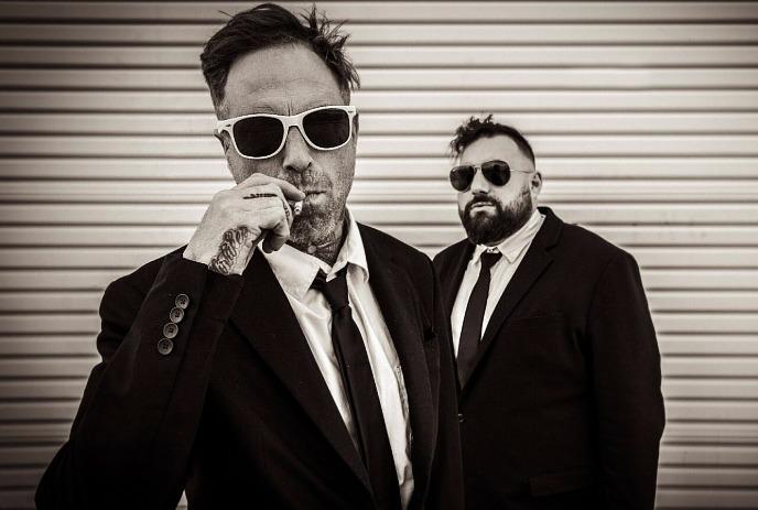 Sam King & Ceschi Ramos in a sepia toned photo, wearing sunglasses and suites posing for the camera.