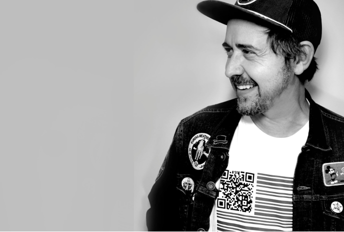 A black and white photo of Danny Michel smiling with his head turned from the camera, wearing a hat against a white background.