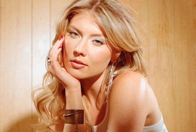 Dasha with her long blonde hair and red nails, posing against a wooden background.