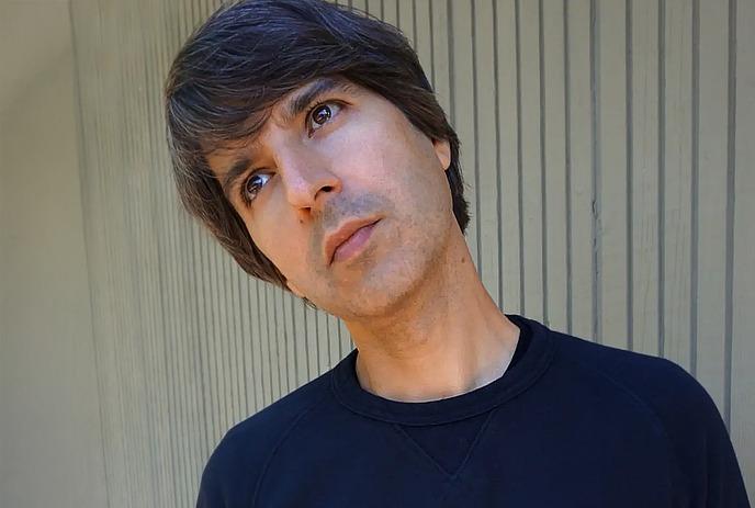 Demetri Martin wearing a long sleeve black shirt, looking up at the sky.