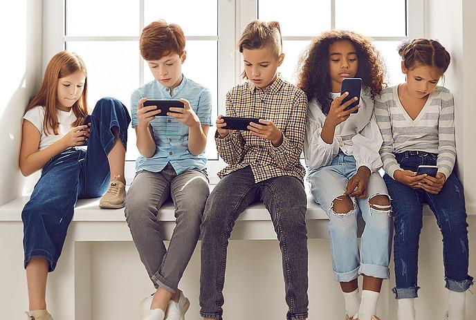 A group of kids sitting on a ledge and staring at their phones