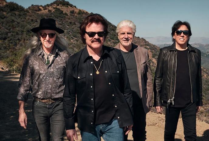 Members of The Doobie Brothers band standing on a dirt road with mountains in the distance