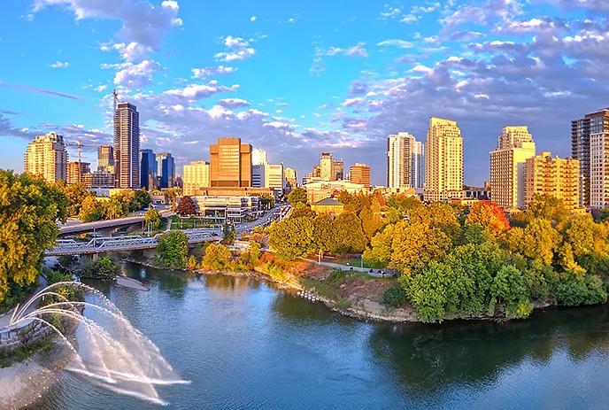 City of London River scene with fountain, autumn trees, and tall sunlit buildings under partly cloudy sky.