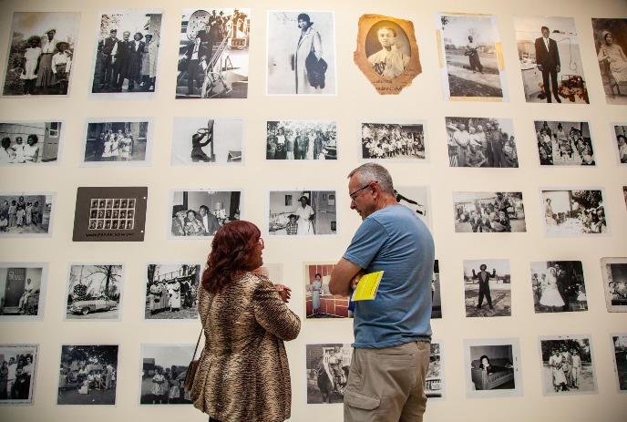 A man and a woman stand in front of a wall filled with different old time pictures.