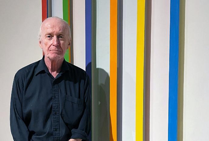 Doug Mitchell standing before bright vertical color stripes in a simple portrait with bold artistic contrast