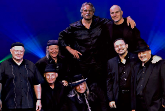 Eight group members dressed in black stand together smiling in front of a blue background.