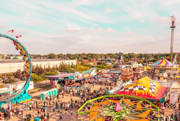 Carnival scene: vibrant rides, colorful tents, crowds enjoying festivities under a partly cloudy sky.