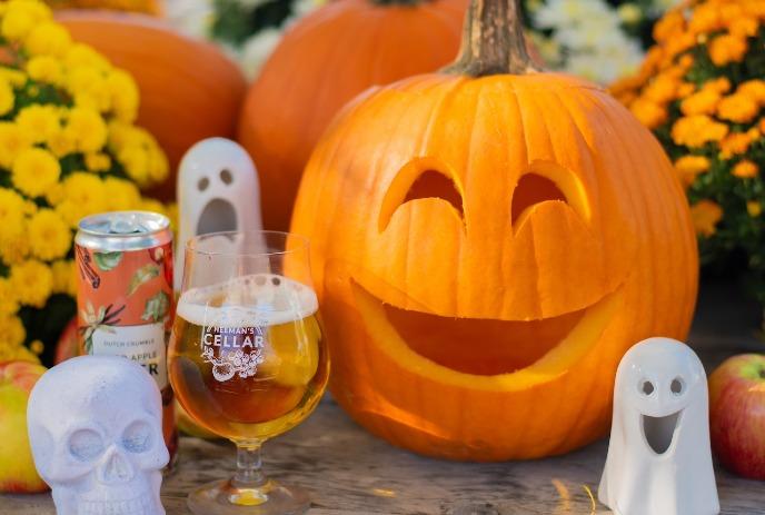 Smiling pumpkin, fall flowers, ghost decor, apples, skull, and citrus cider in a festive autumn setup.