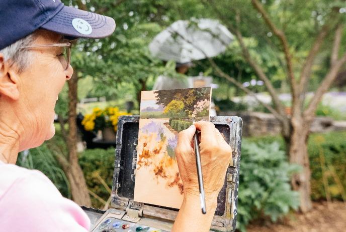 Artist painting a scenic landscape outdoors, capturing nature’s beauty with a brush on canvas.
