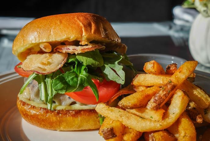 A large burger with all the fixings on a plate with french fries.
