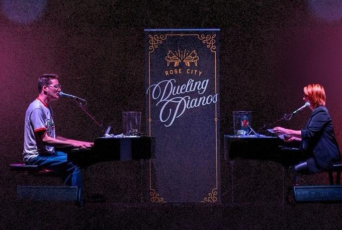 Two people sitting at pianos facing each other.