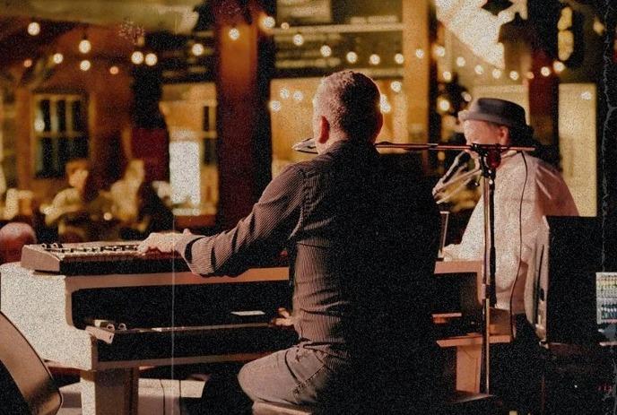Two people playing seperate pianos live on stage