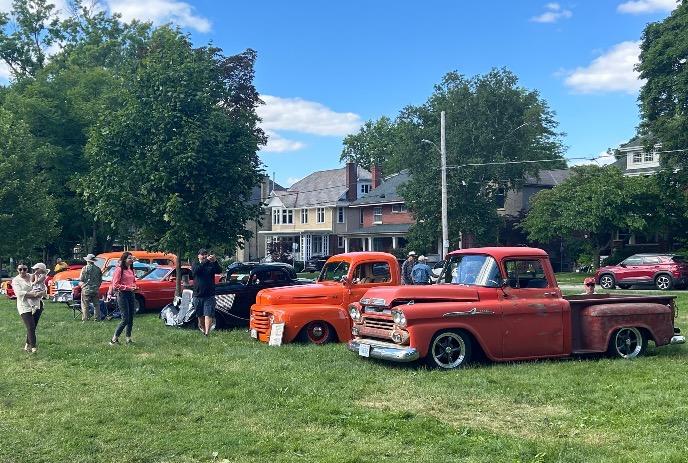 A group of people admire a row of classic trucks and cars displayed on a grassy field.