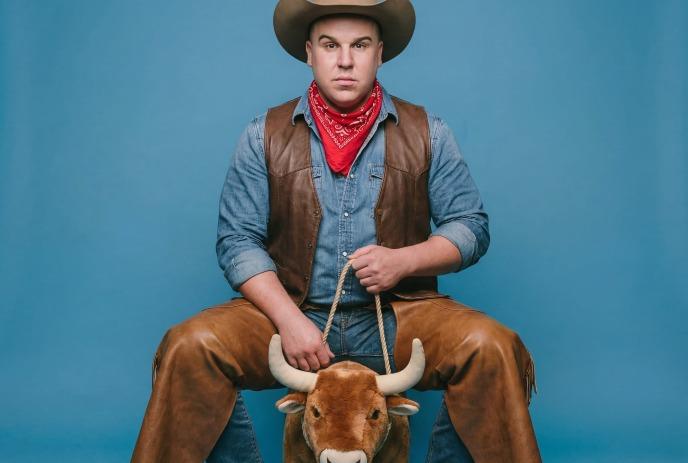Eric Johnston wearing a cowboy outfit riding a toy bull.