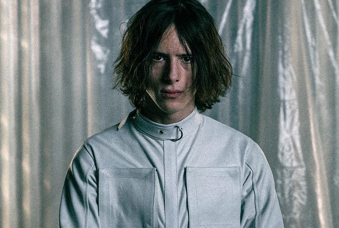 EMORFIK in a straitjacket, looking at the camera with a blank expression.