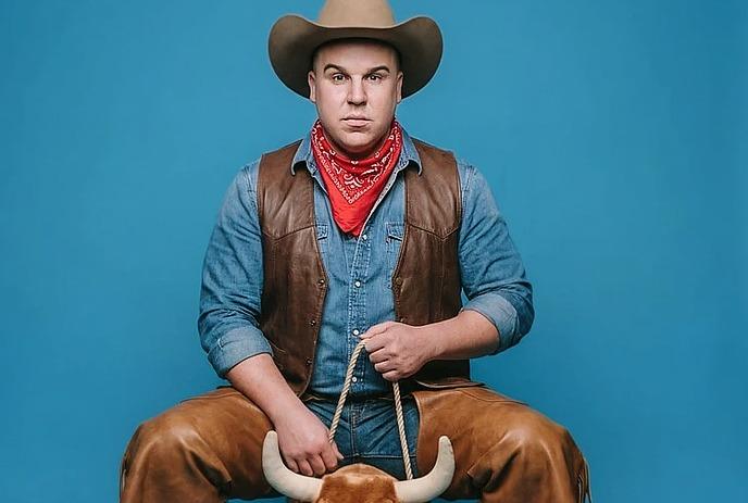 Eric Johnston wearing a cowboy outfit riding a toy bull.