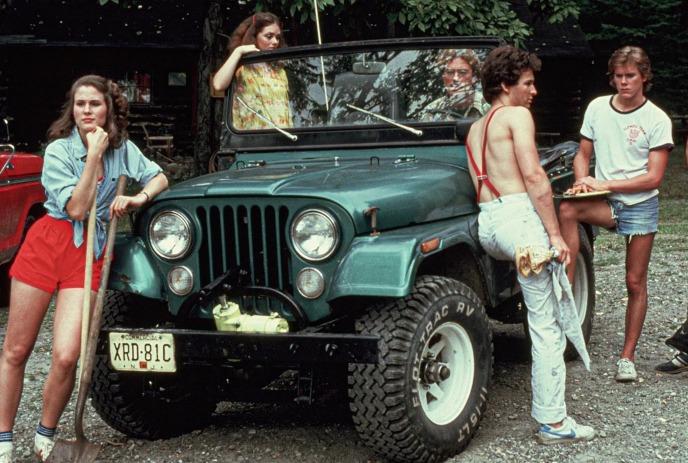 Group of young people hanging around a green jeep.