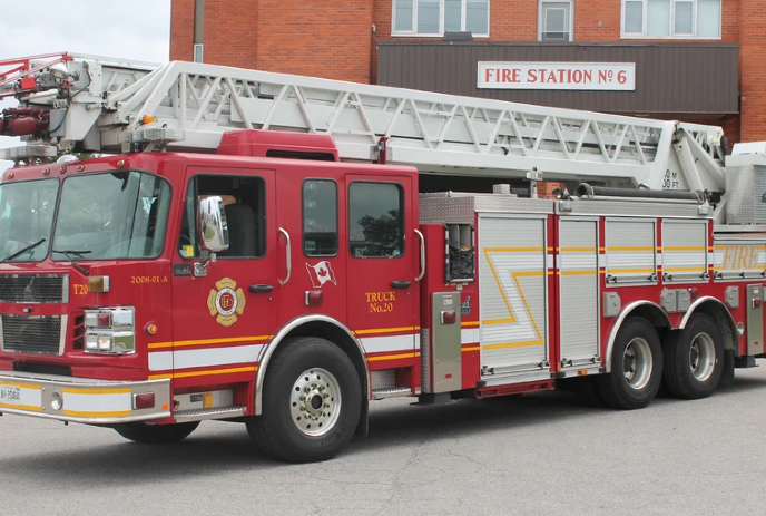Red fire engine with a ladder on top, sitting in front of the fire station.