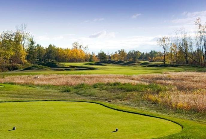 Firerock Golf Club showcases a lush green fairway, rolling hills, and tall grasses, under a clear blue sky.