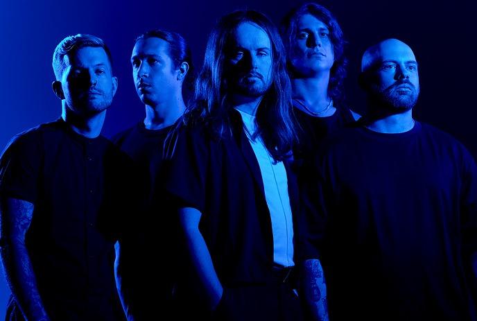 Five band members of Fit for a King stand in a dramatic blue-lit setting, each with serious expressions.