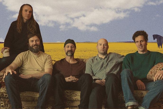 Foxwarren with Hudson Freeman, posed on a vintage couch with golden prairie fields, wildflowers, open sky, and horses.