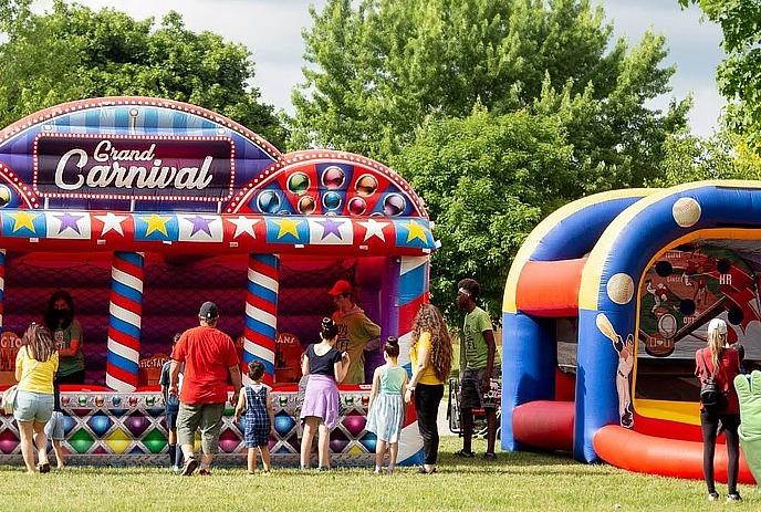 Bouncy castle and carnival games being enjoyed by families outdoors.
