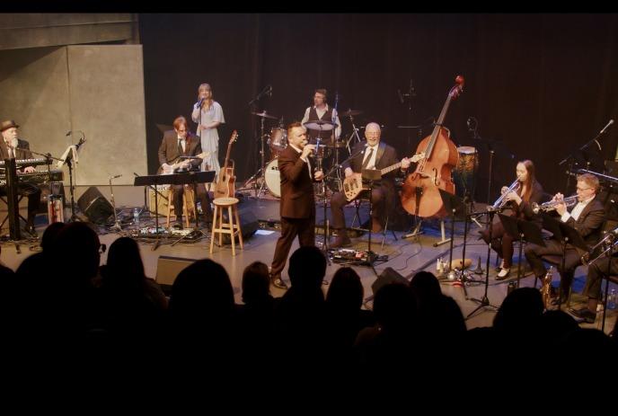 Scott Bollert singing on stage in front of an audience, accompanied by The Jazzman Orchestra.