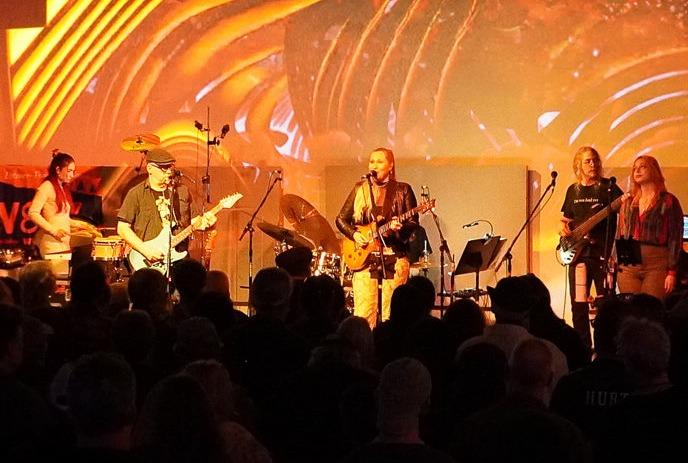 The whole group onstage playing their instruments and singing.