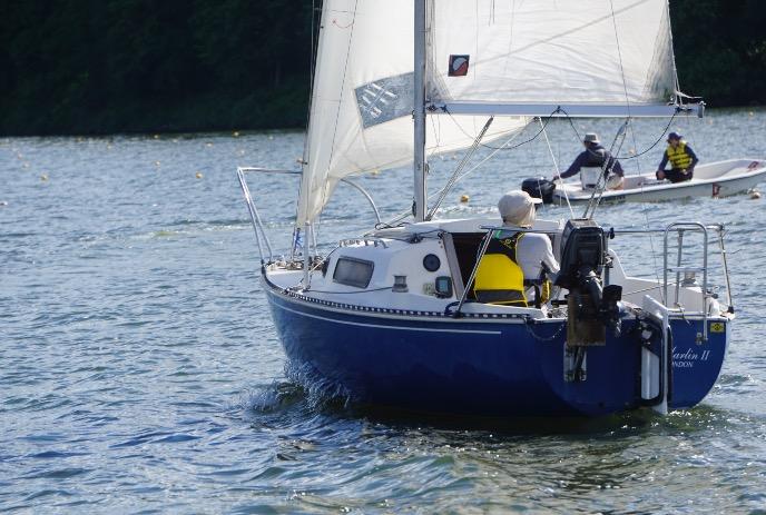 Blue sailboat on the water with a motorboat in front of it.