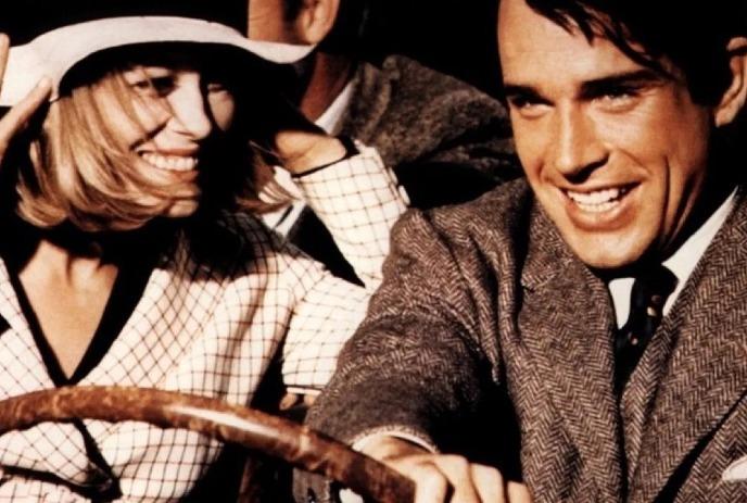 Two people sit smiling in a car wearing vintage clothing sharing a warm joyful moment.