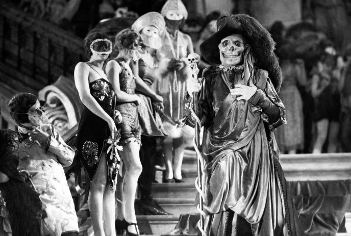 Masked figures in ornate costumes gather on a grand staircase, led by a skeleton-themed character in a dramatic robe.
