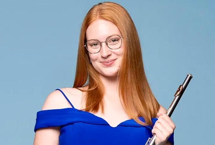 Gillian Derer wearing a dress and smiling, posing against a blueish grey background.