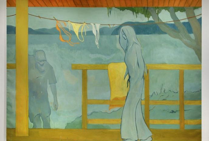 Woman in flowing dress stands on yellow-railed balcony overlooking sea, with hanging laundry and shadowy man in water.